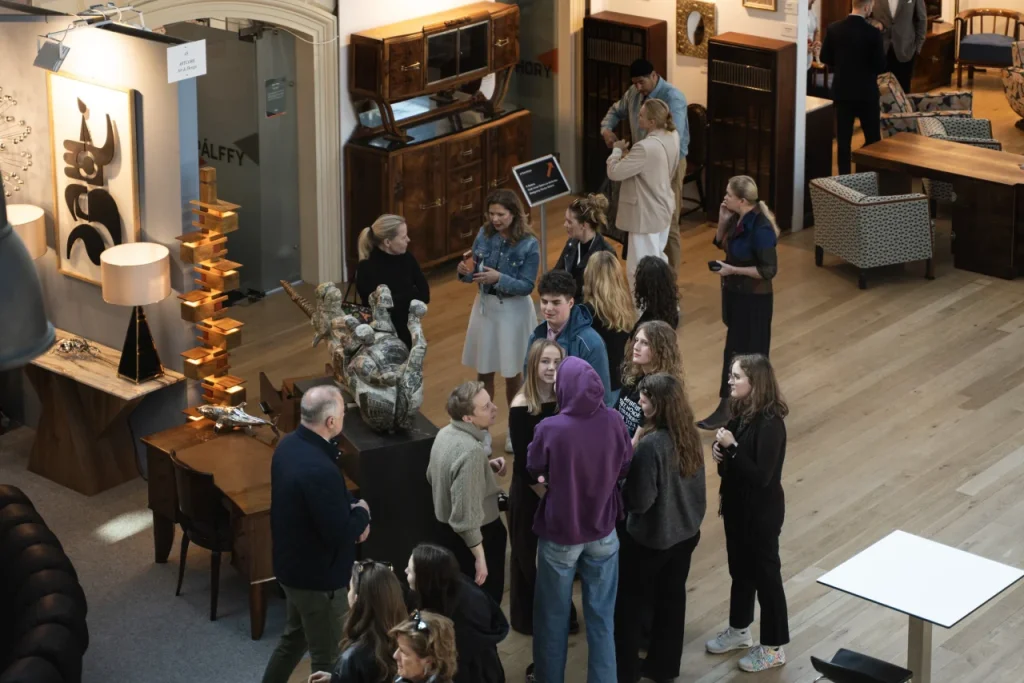 Kiállítás megnyitó: vendégek beszélgetnek szobrok és bútorok között