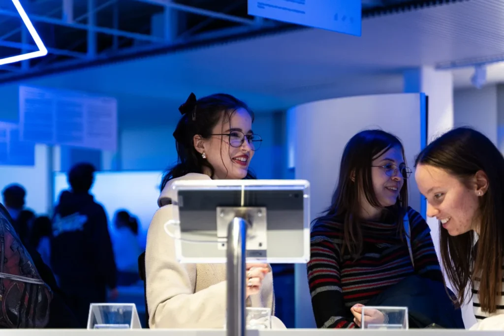 Diákok interaktív kiállítási eszköznél, mosolyogva beszélgetnek